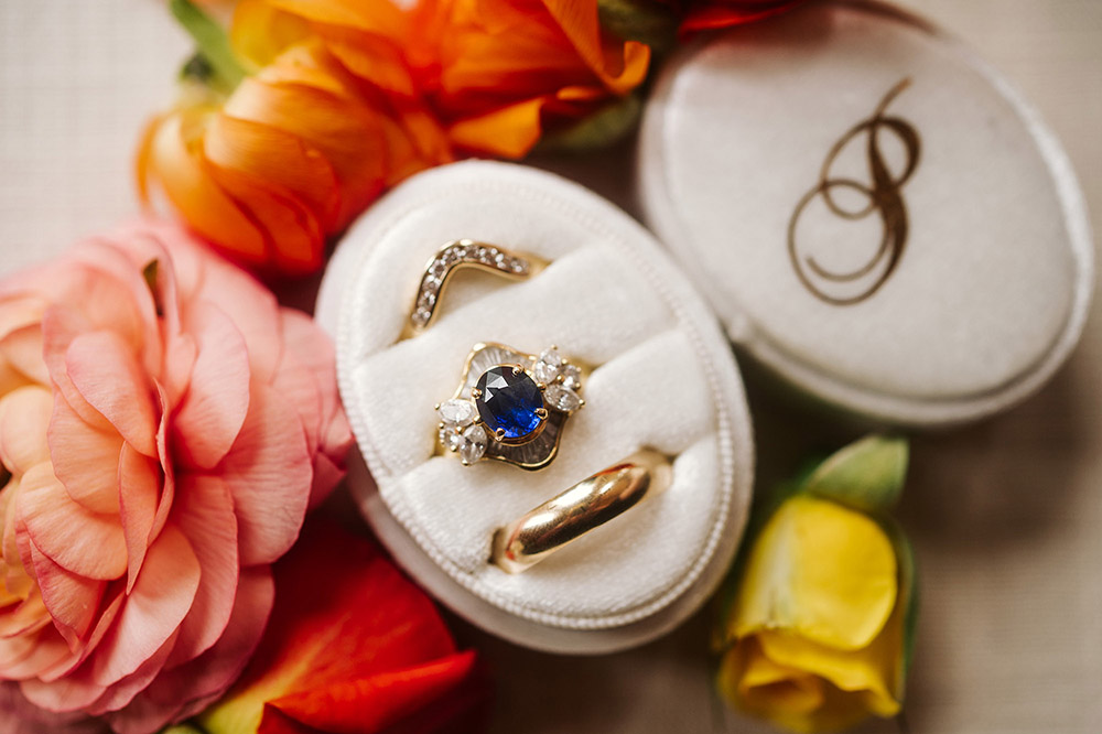 Unique sapphire engagement ring in cream colored ring box surrounded by colorful flowers