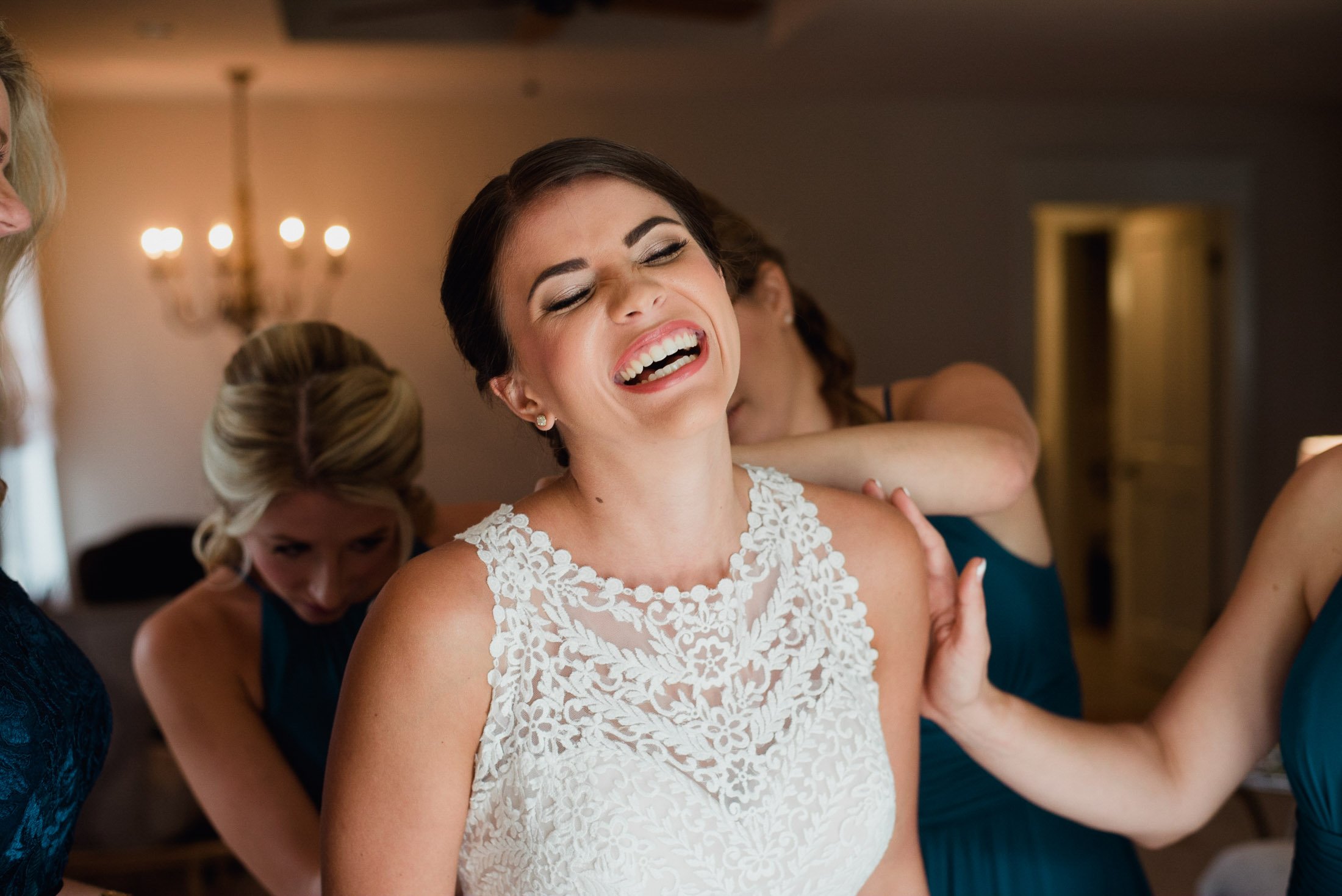 greenhouse at driftwood wedding photographer bride laughing while her bridesmaids get her dressed, natural light photography, bridal suite photos at greenhouse at driftwood, natural, candid wedding photographer in austin texas