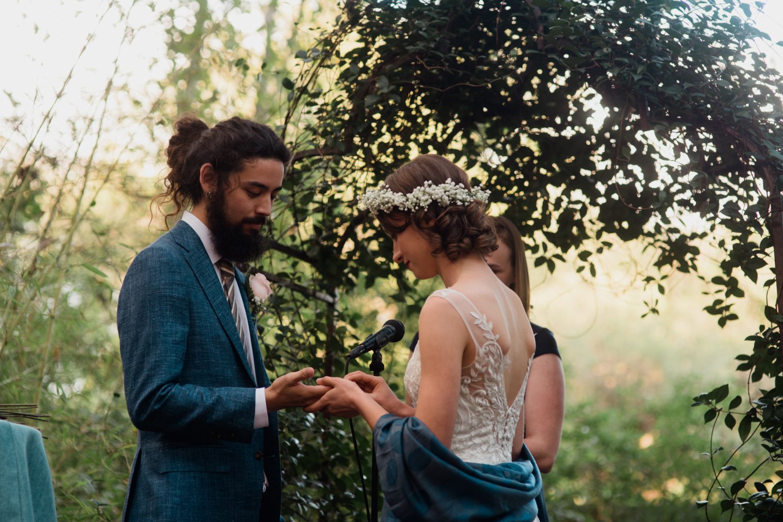 bride and groom exchange rings in front of a greenery archway at their Fall Austin, Texas wedding