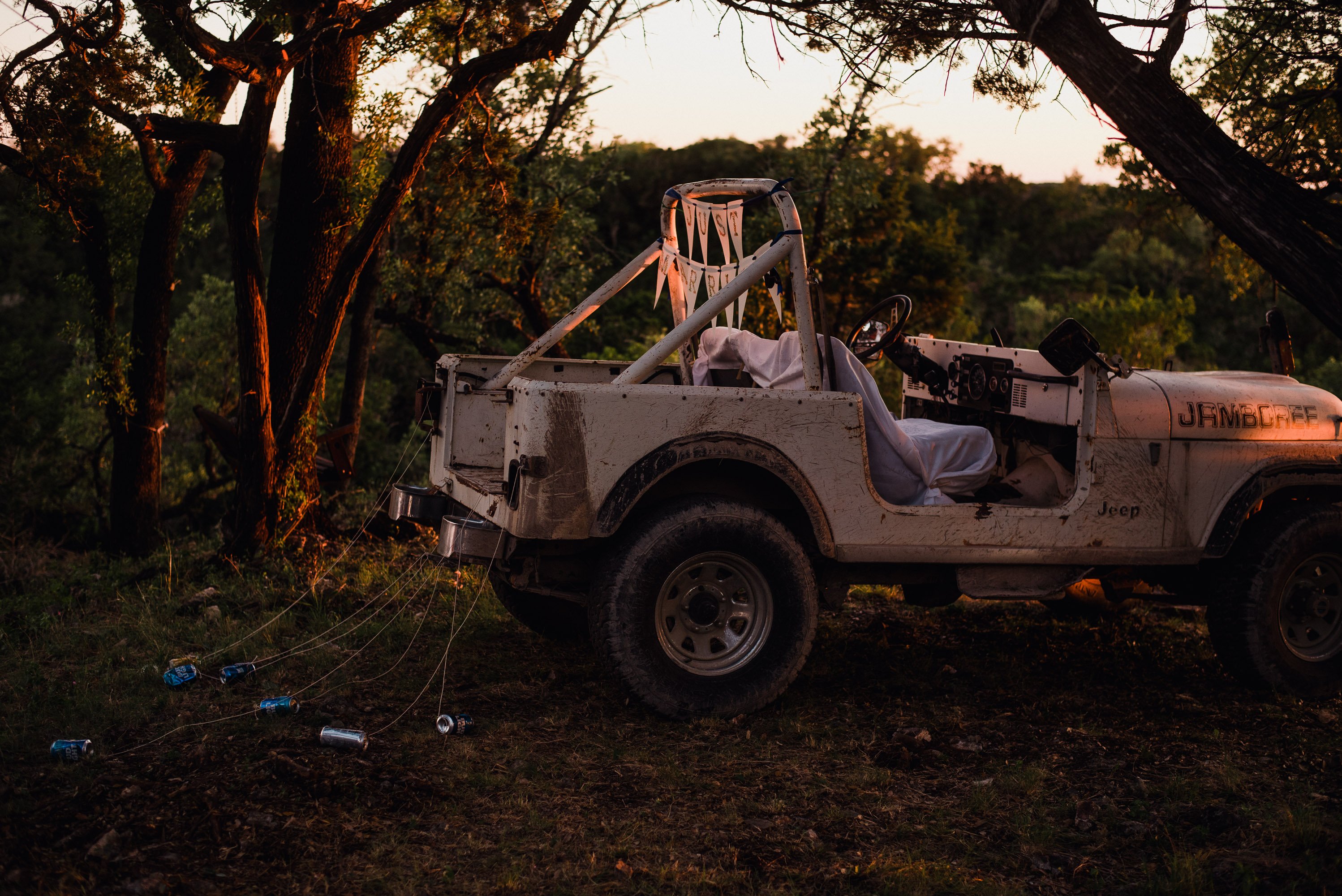 a vintage white jeep with a "just married banner" and beer cans tied to the bumper