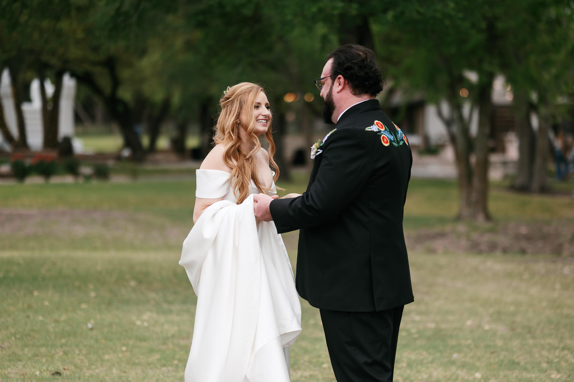 first look between bride and groom at their Ranch Austin Wedding in Texas. Groom wears a custom embroidered black suit with native wildflowers on the back