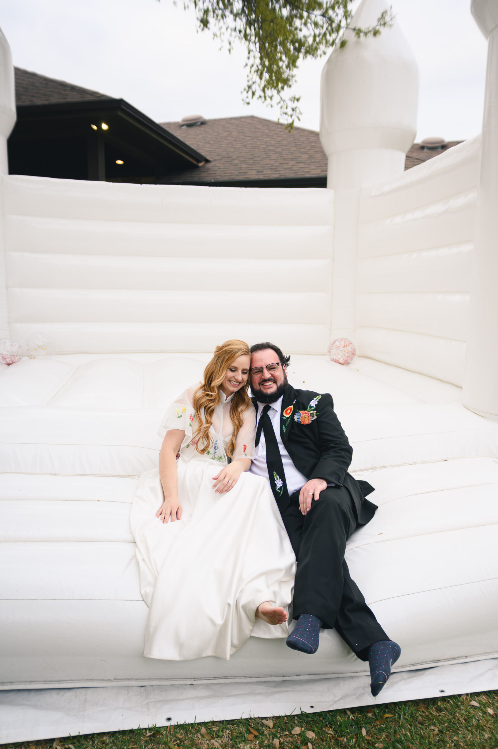 bride and groom sit together at the edge of a white bounce house