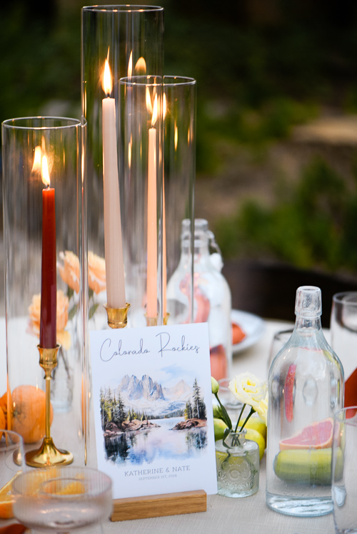 Elegant table setting featuring tall candle flames in glass holders, pastel flowers, and a centerpiece table marker card, creating a warm, inviting atmosphere.