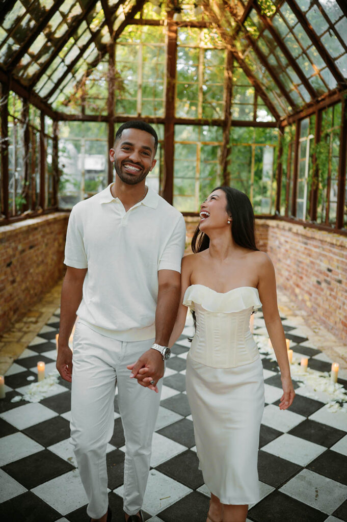 newley engaged couple walking and laughing in a glass green house with a checkerboard floor